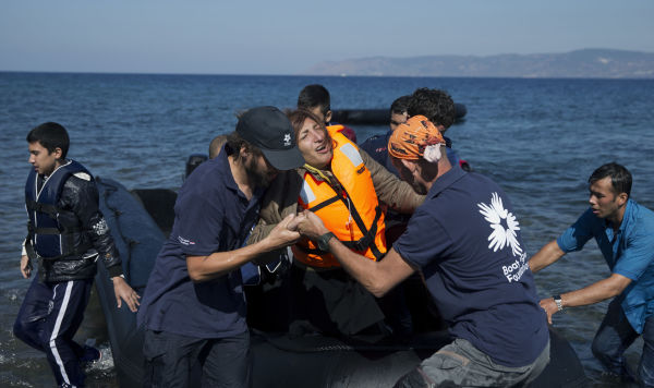 Добровольцы помогают женщине после того, как она прибыла на лодке из Турции на остров Лесбос, Греция, 2015 год