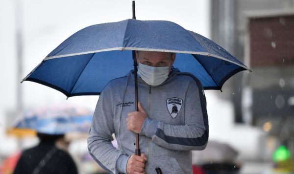Мужчина в медицинской маске под зонтом