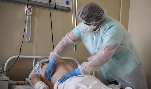 Медицинский работник у кровати пациента в отделении для больных коронавирусом COVID-19