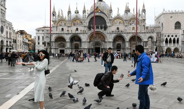 Туристы фотографируются с голубями перед собором Сан-Марко в Венеции