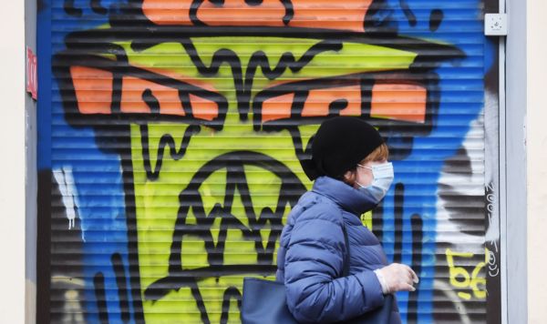 Женщина в защитной маске проходит рядом со зданием с граффити