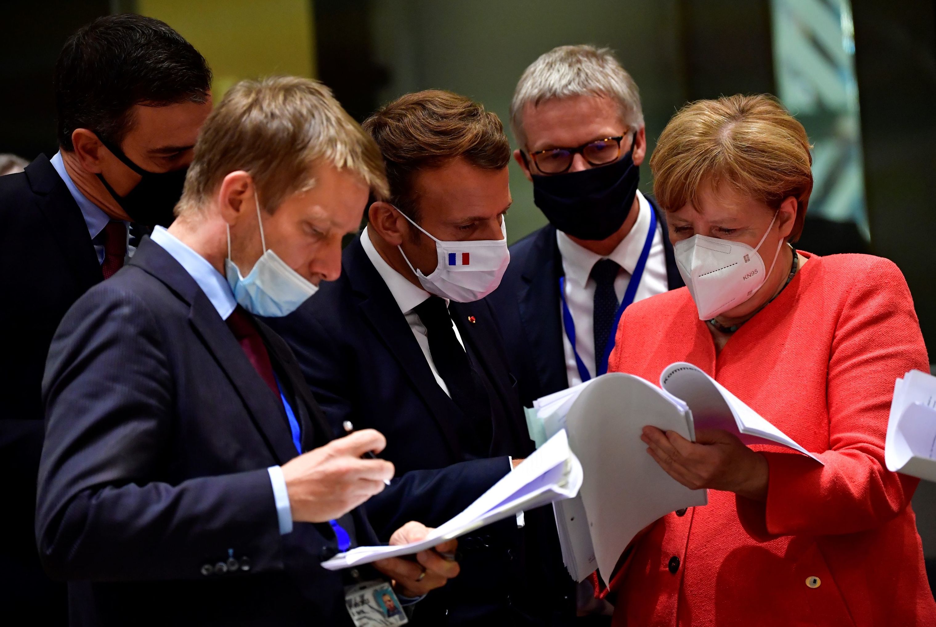Премьер-министр Испании Педро Санчес (слева), президент Франции Эммануэль Макрон (слева) и канцлер Германии Ангела Меркель (справа) рассматривают документы во время саммита ЕС в Брюсселе 20 июля 2020 года