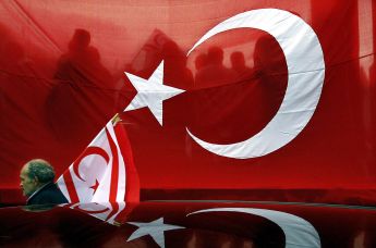 Турецкий поселенец-киприот с флагом Турецкой республики Северного Кипра на фоне гигантского турецкого флага