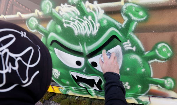 Художник рисует граффити, изображающее борьбу вакцины с коронавирусом