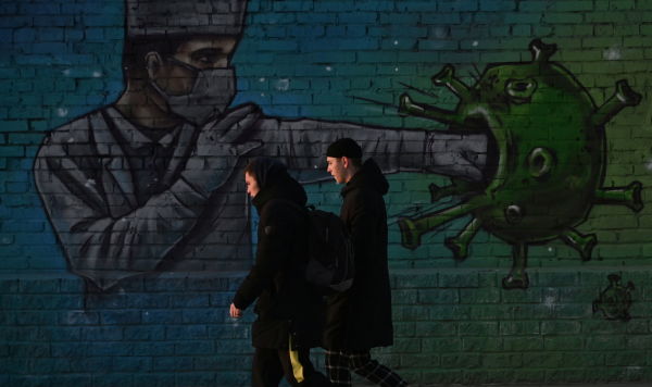 Молодые люди проходят мимо граффити с изображением борющегося с коронавирусом медицинского работника