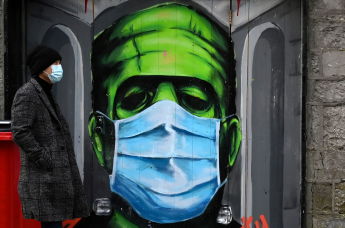 Мужчина проходит мимо граффити с изображением Франкенштейна в защитной маске