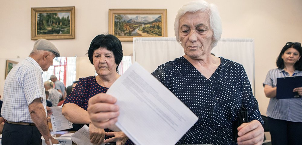 Женщина опускает бюллетень в урну для голосования на парламентских выборах в Южной Осетии